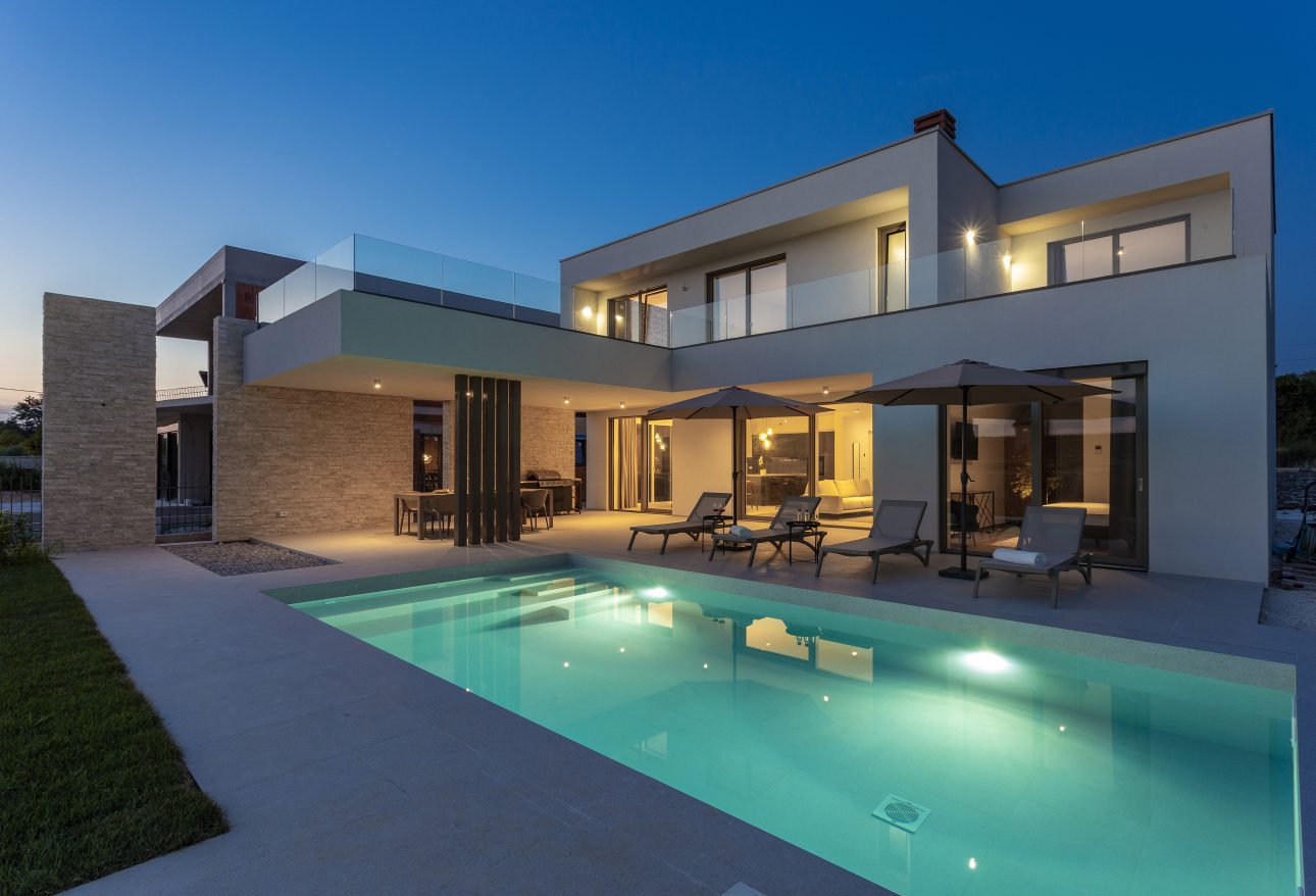a pool and a house with chairs and umbrellas in Rovinj