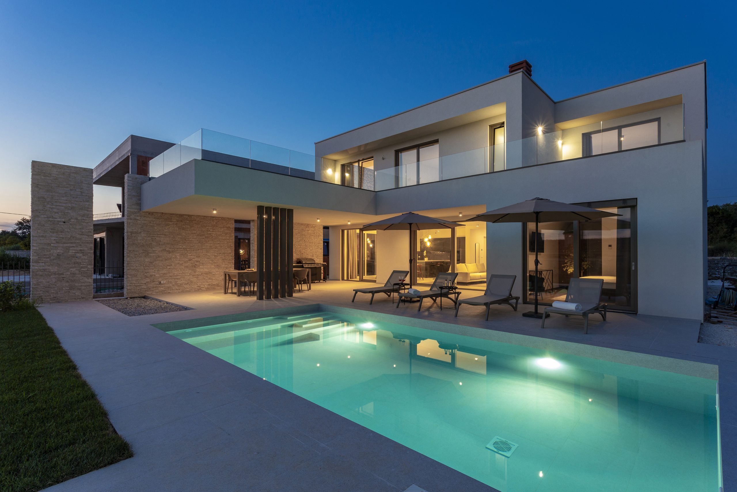 a pool and a house with chairs and umbrellas in Rovinj